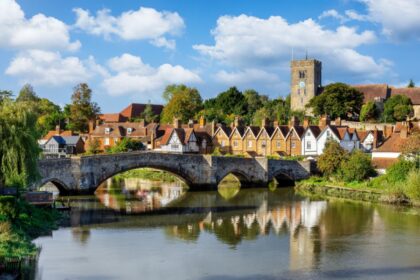 Panoramic view of Aylesford village in Kent, England with medieval bridge over the river Medway and church behind with ablue sky and fluffy white clouds