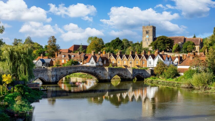 Panoramic view of Aylesford village in Kent, England with medieval bridge over the river Medway and church behind with ablue sky and fluffy white clouds