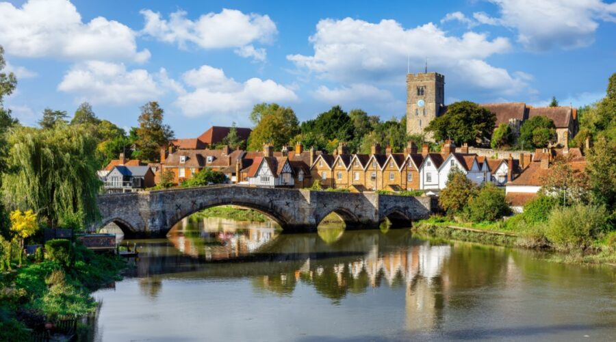 Panoramic view of Aylesford village in Kent, England with medieval bridge over the river Medway and church behind with ablue sky and fluffy white clouds