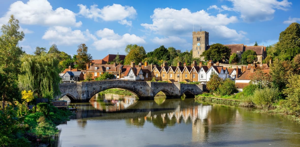 Panoramic view of Aylesford village in Kent, England with medieval bridge over the river Medway and church behind with ablue sky and fluffy white clouds