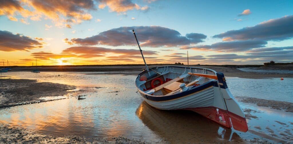Stunning sunset over a fishing boat at Burnham Overy Staithe on the Norfolk Coast. Image by Helen Hotson / Shutterstock