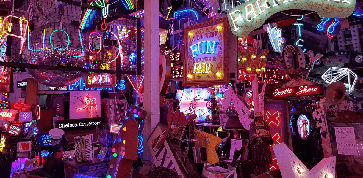 A colourful jumble of neon signs at God’s Own Junkyard in Walthamstow, London, featuring glowing slogans, vintage advertisements, and salvaged lights packed into a vibrant indoor display.