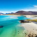 A beautiful sandy beach and clear turquoise sea with mountains in the background, on the Isle of Harris in the Western isles of Scotland