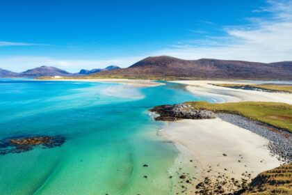 A beautiful sandy beach and clear turquoise sea with mountains in the background, on the Isle of Harris in the Western isles of Scotland