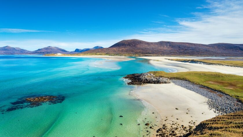 A beautiful sandy beach and clear turquoise sea with mountains in the background, on the Isle of Harris in the Western isles of Scotland