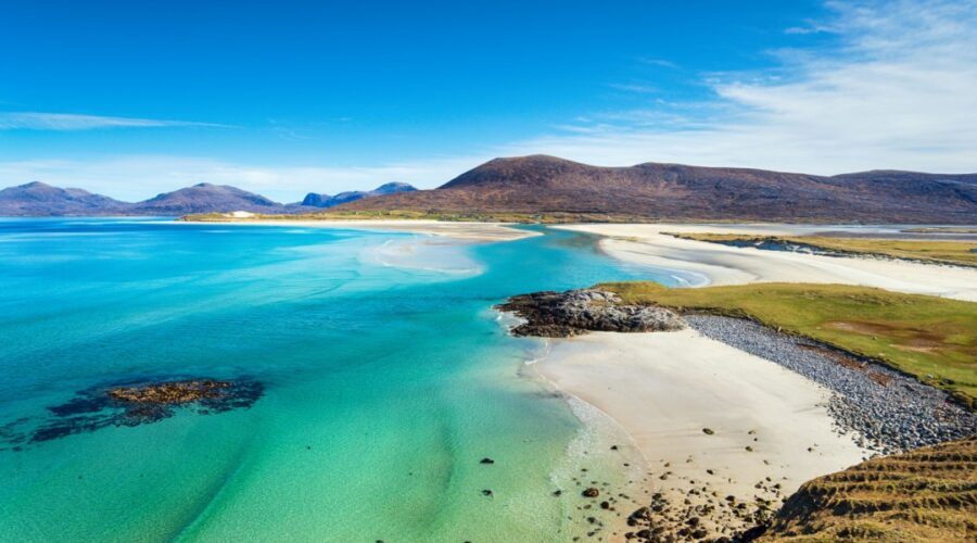 A beautiful sandy beach and clear turquoise sea with mountains in the background, on the Isle of Harris in the Western isles of Scotland