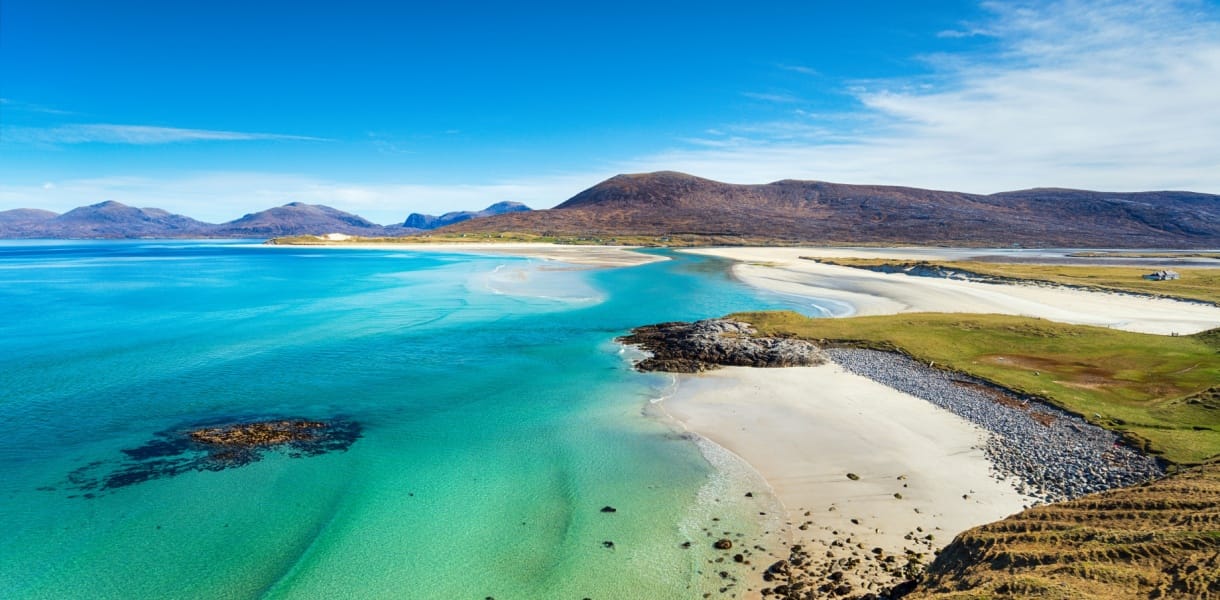 A beautiful sandy beach and clear turquoise sea with mountains in the background, on the Isle of Harris in the Western isles of Scotland