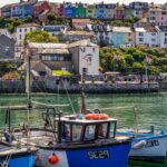 Small fishing boats in a harbour at Brixham with pastel coloured cotatges on the hillside in the background. Devon, England