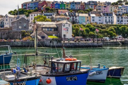 Small fishing boats in a harbour at Brixham with pastel coloured cotatges on the hillside in the background. Devon, England
