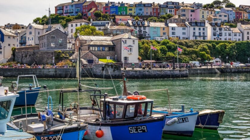 Small fishing boats in a harbour at Brixham with pastel coloured cotatges on the hillside in the background. Devon, England