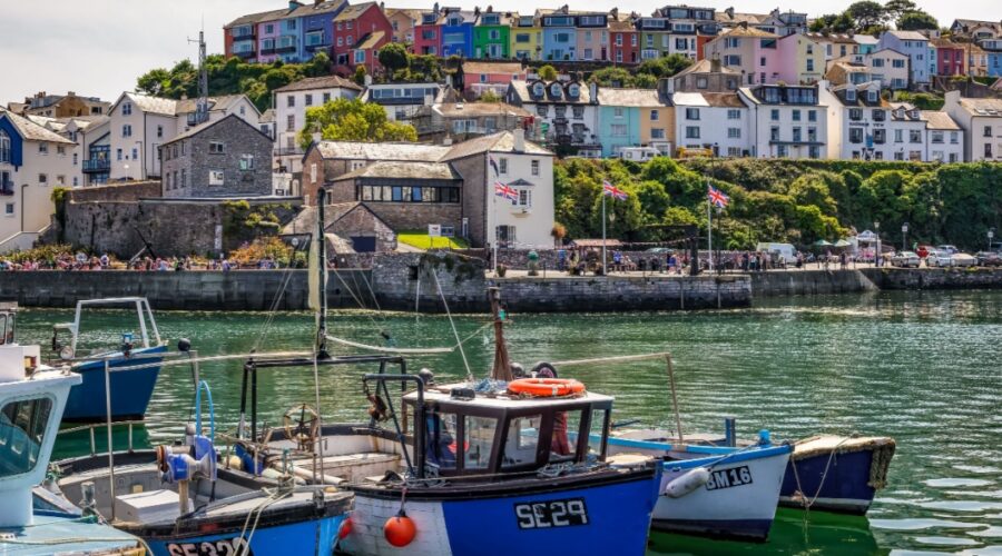 Small fishing boats in a harbour at Brixham with pastel coloured cotatges on the hillside in the background. Devon, England