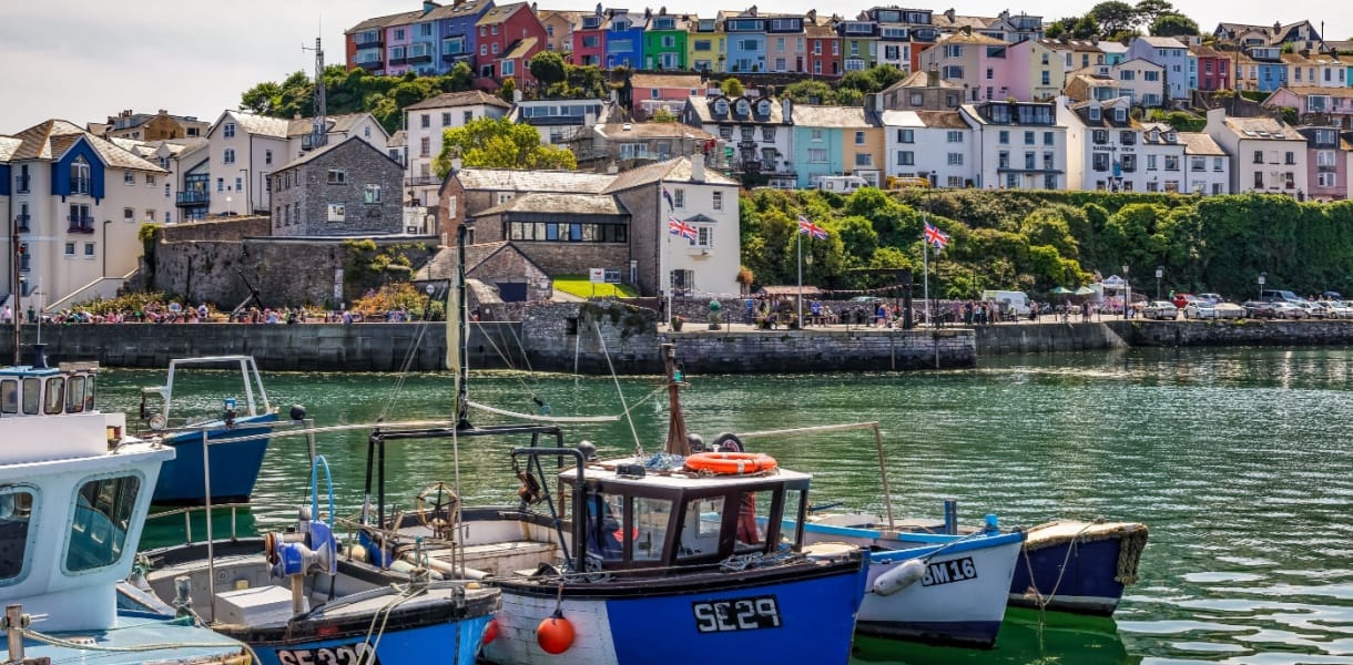 Small fishing boats in a harbour at Brixham with pastel coloured cotatges on the hillside in the background. Devon, England