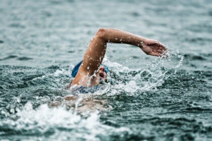 Wild Swimming in South East England.Open-water swimmer in a blue cap and goggles performing a front-crawl stroke, arm outstretched and water spraying amid dark, choppy waves