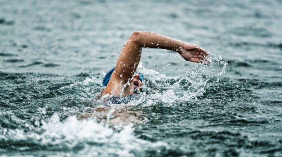 Wild Swimming in South East England.Open-water swimmer in a blue cap and goggles performing a front-crawl stroke, arm outstretched and water spraying amid dark, choppy waves
