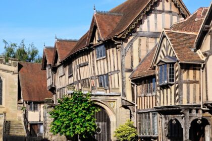 Historic timber-framed buildings in Warwick, England, including the Lord Leycester Hospital, with gabled roofs and leaded windows under a bright blue sky. The medieval architecture is well-preserved and richly detailed, showcasing the town’s centuries-old character.