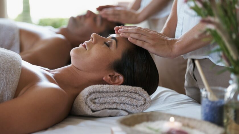 A woman and man lying side by side on massage beds receiving head massages at a luxury hotel spa, surrounded by soft towels and calming decor.