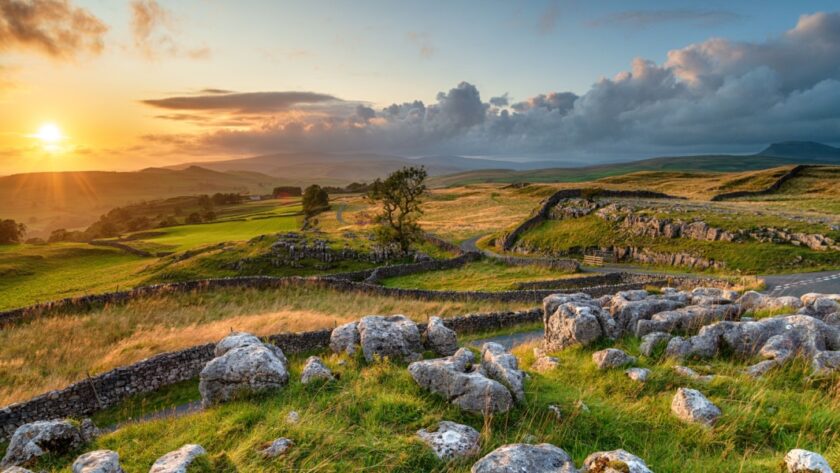 Sunset over the rolling hills and dry-stone walls of the Yorkshire Dales, with rocky foreground, winding dry stone walls, and a golden sky casting warm light across the landscape