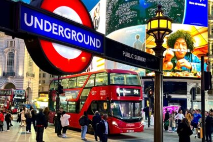 London, Piccadilly Circus at dusk with crowds, red double-decker buses, and illuminated billboards, including a bright Underground sign in the foreground.