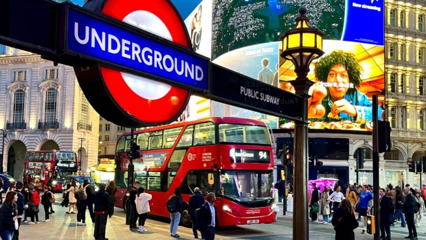 London, Piccadilly Circus at dusk with crowds, red double-decker buses, and illuminated billboards, including a bright Underground sign in the foreground.