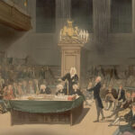 Historic painting of the House of Commons in the late 18th century, showing a crowded parliamentary session with men in period dress seated on benches and gathered around a central table. A speaker stands addressing the chamber while others listen attentively. The scene captures the era of William Wilberforce and the abolition debates, with candlelight illuminating the ornate wooden interior and royal crest above the speaker's chair.