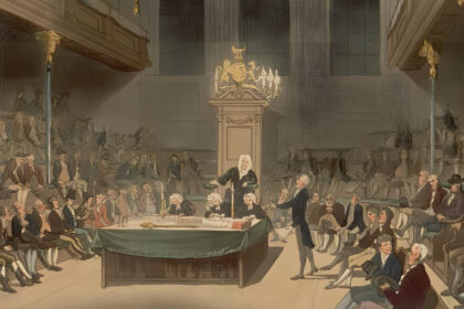 Historic painting of the House of Commons in the late 18th century, showing a crowded parliamentary session with men in period dress seated on benches and gathered around a central table. A speaker stands addressing the chamber while others listen attentively. The scene captures the era of William Wilberforce and the abolition debates, with candlelight illuminating the ornate wooden interior and royal crest above the speaker's chair.