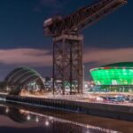 Night view of the Glasgow waterfront featuring the illuminated SEC Armadillo and OVO Hydro venues, with the historic Finnieston Crane and reflections on the River Clyde.