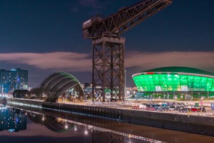 Night view of the Glasgow waterfront featuring the illuminated SEC Armadillo and OVO Hydro venues, with the historic Finnieston Crane and reflections on the River Clyde.