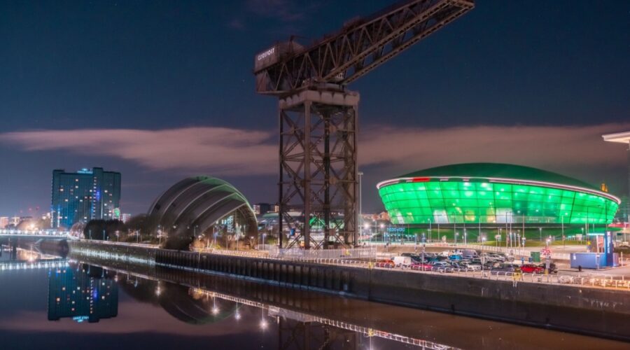 Night view of the Glasgow waterfront featuring the illuminated SEC Armadillo and OVO Hydro venues, with the historic Finnieston Crane and reflections on the River Clyde.