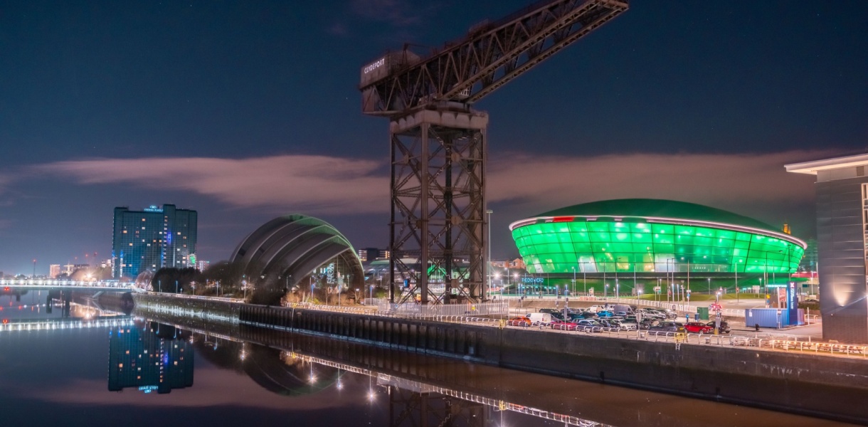 Night view of the Glasgow waterfront featuring the illuminated SEC Armadillo and OVO Hydro venues, with the historic Finnieston Crane and reflections on the River Clyde.