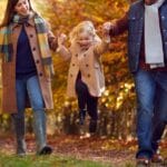 Excited Girl Being Swung By Parents On Family Autumn Walk Through Countryside