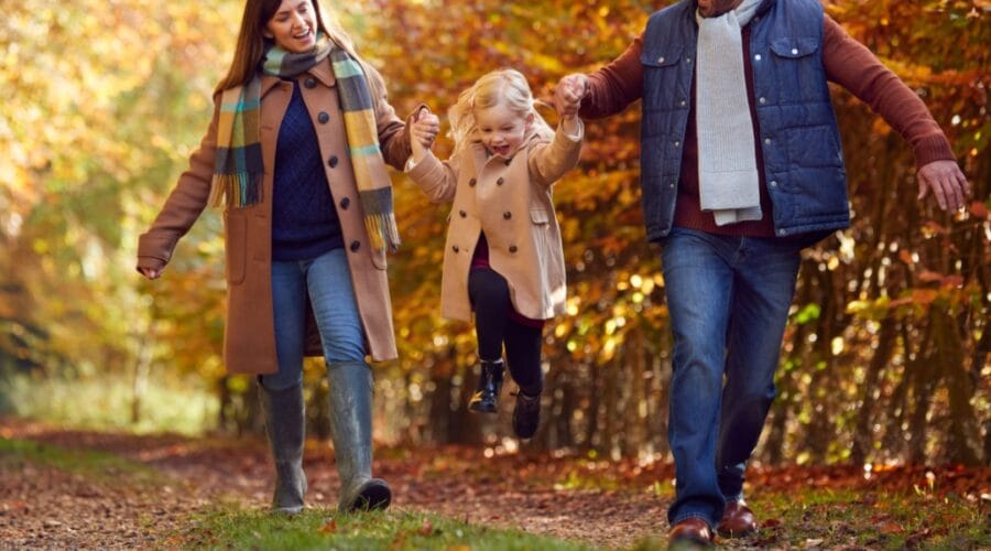 Excited Girl Being Swung By Parents On Family Autumn Walk Through Countryside