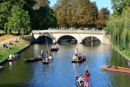 Visitors punting on the River Cam in Cambridge, gliding past the historic Clare Bridge with students and tourists relaxing on the riverbanks, a classic Cambridge weekend experience.