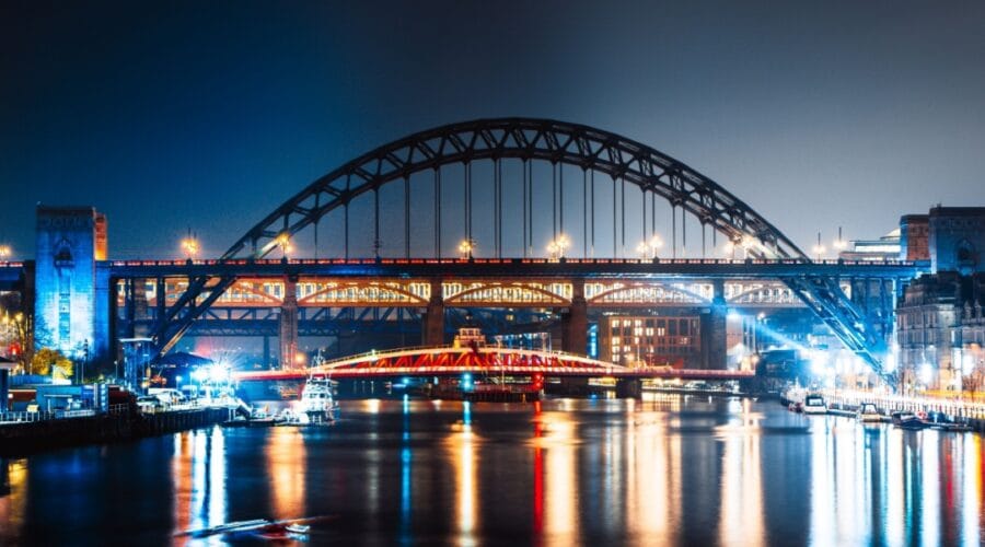 Night view of Newcastle Quayside with the illuminated Tyne Bridge, Swing Bridge, and High Level Bridge reflecting on the River Tyne