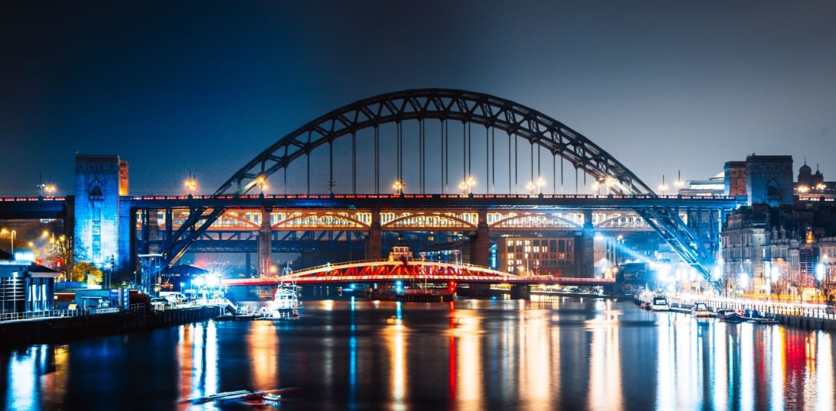 Night view of Newcastle Quayside with the illuminated Tyne Bridge, Swing Bridge, and High Level Bridge reflecting on the River Tyne