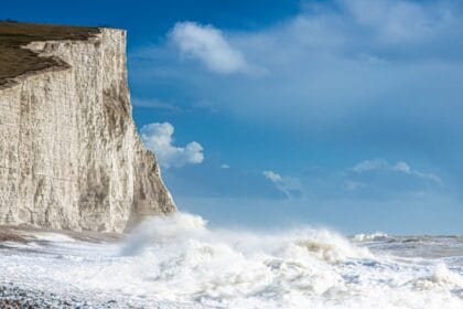 The iconic chalk cliffs of the Seven Sisters rise starkly from the Sussex coastline, their gleaming white faces contrasting against a deep blue sky and the churning waves below. Towering, sheer, and weather-beaten by centuries of sea spray, the cliffs create one of England’s most dramatic coastal views, where walkers trace the narrow paths above and the restless Channel pounds the shingle shore beneath