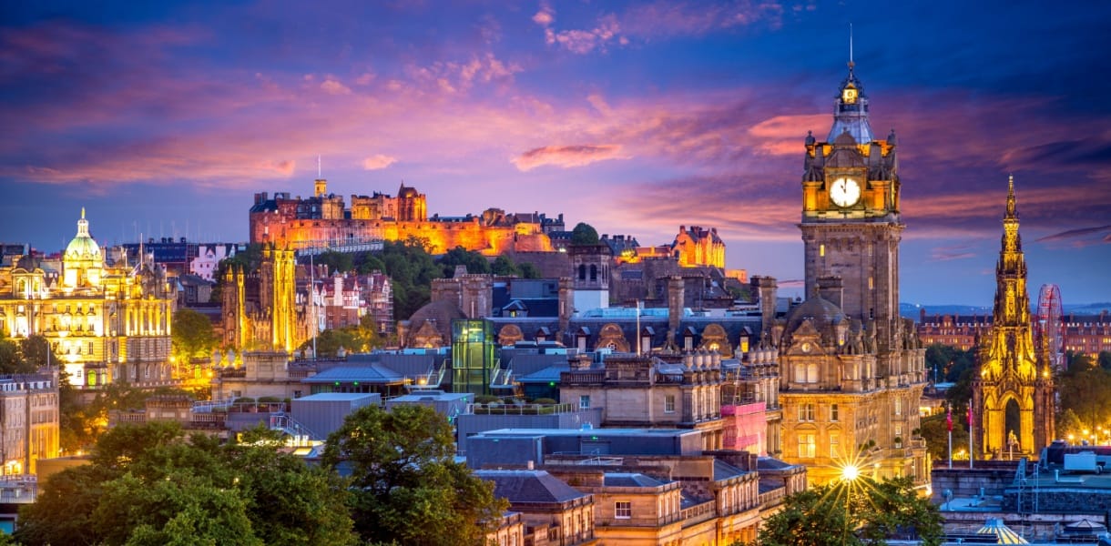 Edinburgh skyline at dusk with Edinburgh Castle, historic buildings, and illuminated clock tower under a colourful evening sky.