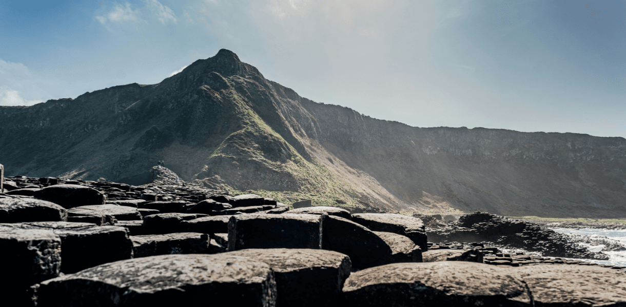 Basalt columns at Giant’s Causeway on the Antrim Coast, with rugged cliffs and hills rising behind in bright summer light.