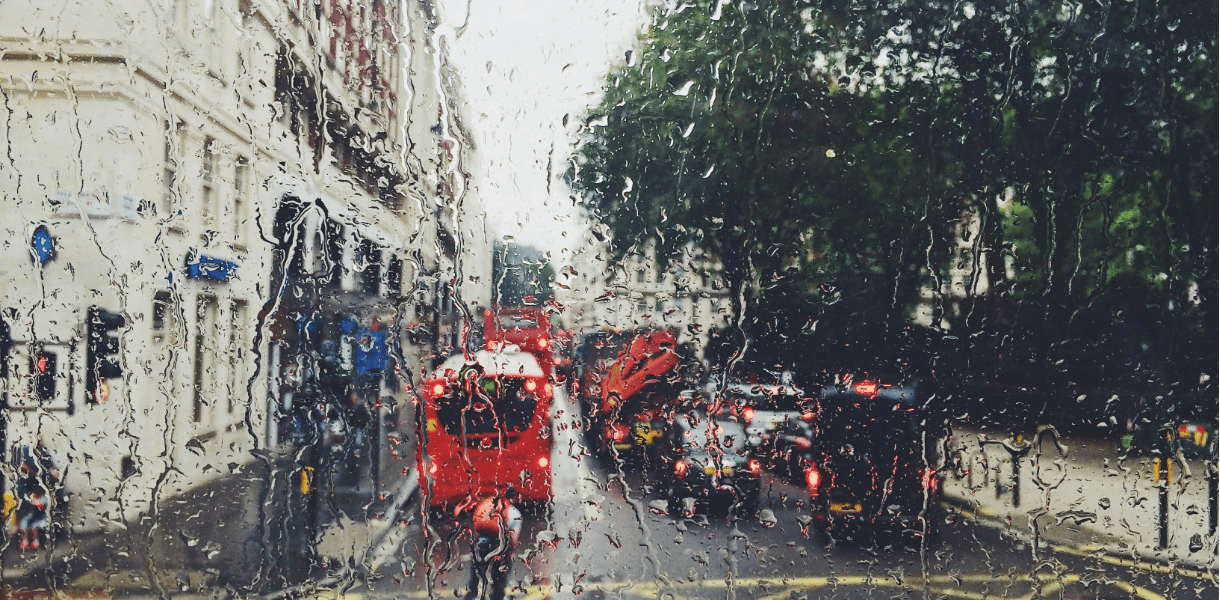 View of a rainy london street from the front seat of a london bus with raindrops steaking the glass.