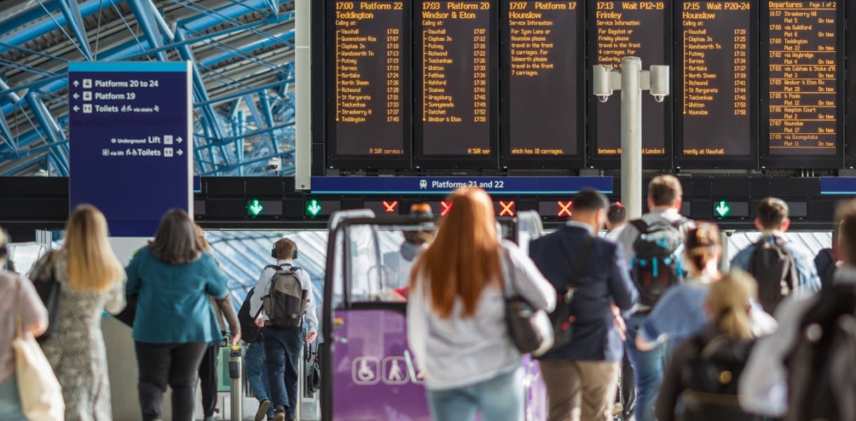 Commuters and travellers walk beneath departure boards and platform signs inside London Waterloo station.