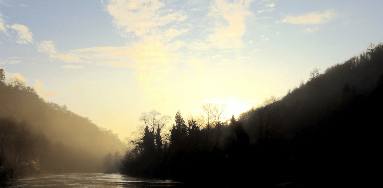 Misty Wye Valley river at sunset with wooded hills silhouetted against a pale golden sky.
