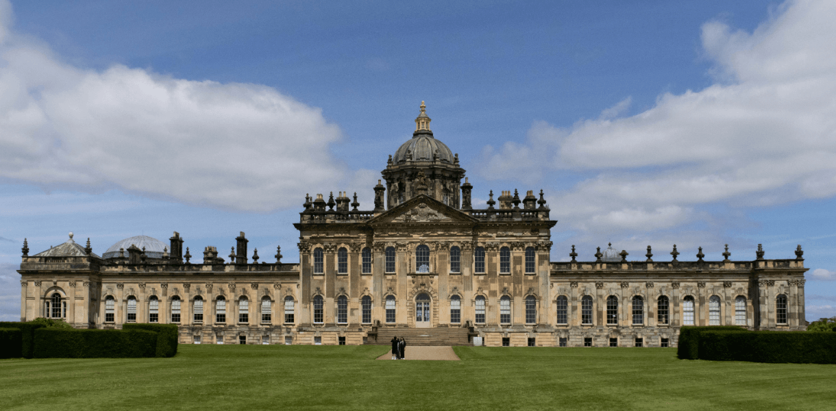 Castle Howard in North Yorkshire, with its grand domed façade, formal lawns and clipped hedges beneath a blue sky with scattered clouds.
